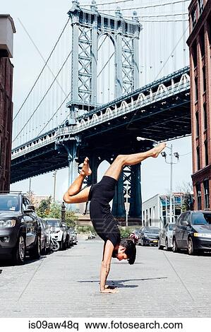 Stock Photography - Man practising yoga handstand in front of Manhattan Bridge, New York, USA. Fotosearch