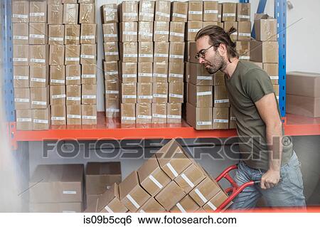 Man pushing sack trolley of stacked cardboard boxes in factory View Large Photo Image Stock Photograph - Man pushing sack trolley of stacked cardboard boxes in factory. Fotosearch