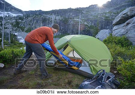 Stock Image - Man putting sleeping bag in tent at sunset, Fault Lake, Selkirk Mountains, Idaho. Fotosearch