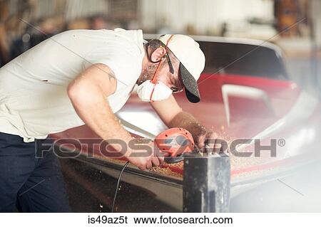 Stock Photograph - Man sanding bodywork in boat repair workshop. Fotosearch