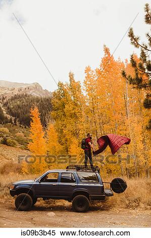 Stock Photography - Man shaking sleeping bag on top of vehicle in autumn forest, Mineral King, Sequoia National Park, California, USA. Fotosearch