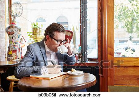 Man sitting in cafe, drinking coffee, writing in notebook View Large Photo Image Stock Image - Man sitting in cafe, drinking coffee, writing in notebook. Fotosearch