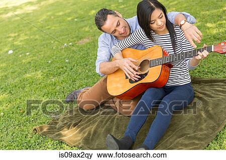Man sitting on grass teaching woman to play acoustic guitar View Large Photo Image Stock Photo - Man sitting on grass teaching woman to play acoustic guitar. Fotosearch