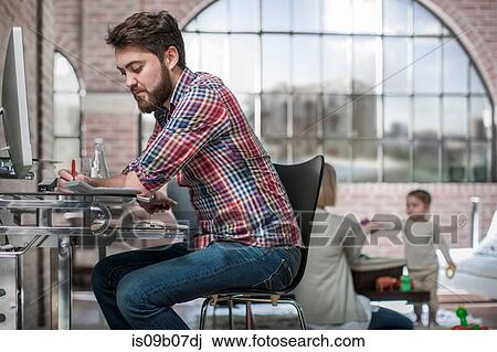 Man sitting working at desk, young woman playing with toddler behind him View Large Photo Image Stock Image - Man sitting working at desk, young woman playing with toddler behind him. Fotosearch