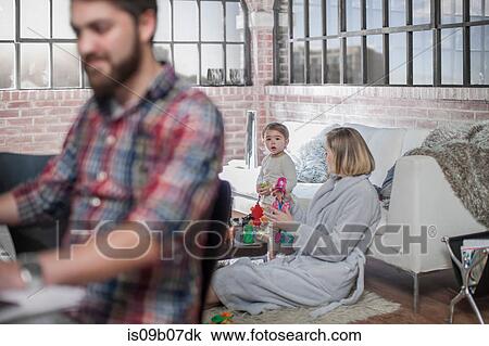 Man sitting working at desk, young woman playing with toddler behind him View Large Photo Image Stock Image - Man sitting working at desk, young woman playing with toddler behind him. Fotosearch