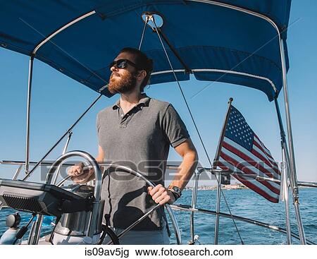 Stock Image - Man steering wheel of sailboat, San Diego Bay, California, USA. Fotosearch