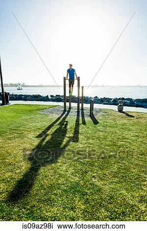 Stock Image - Man training, doing push ups on exercise bars at coast, downtown San Diego, California, USA. Fotosearch