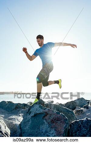 Stock Image - Man training, running on sunlit coast rocks, downtown San Diego, California, USA. Fotosearch