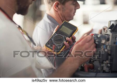 Stock Photo - Man using machine to test outboard motor in boat repair workshop. Fotosearch