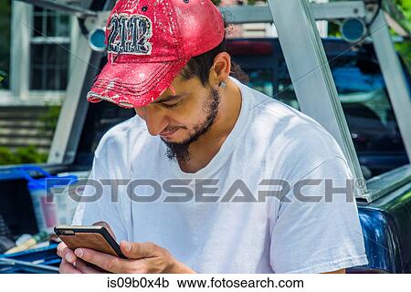 Stock Image - Man wearing baseball cap using smartphone. Fotosearch