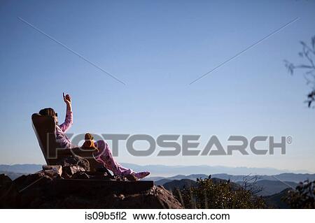 Stock Image - Man wearing pink onesie sunbathing with teddy bear, Malibu Canyon, California, USA. Fotosearch