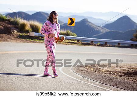 Stock Image - Man wearing pink onesie walking in road carrying teddybear, Malibu Canyon, California, USA. Fotosearch