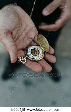 Stock Photography - Man wearing suit, holding pocket watch in hand, elevated view, close-up. Fotosearch