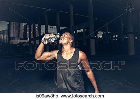 Stock Photography - Man wearing vest drinking water from plastic bottle smiling. Fotosearch