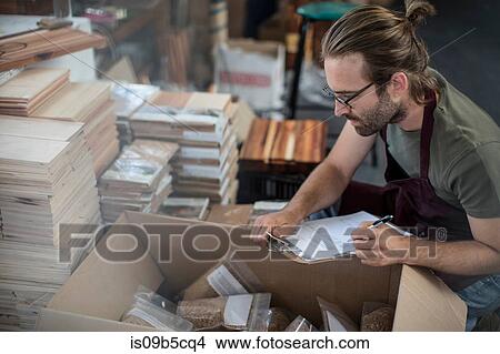 Man with clipboard checking boxed products in factory View Large Photo Image Picture - Man with clipboard checking boxed products in factory. Fotosearch