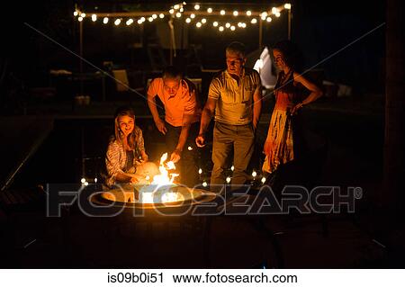Stock Image - Mature adult couples toasting marshmallows on patio fire at night. Fotosearch