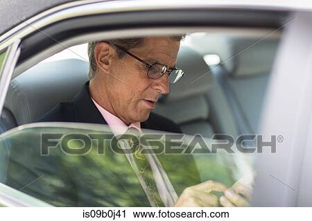 Mature businessman in back of car, using smartphone View Large Photo Image Stock Image - Mature businessman in back of car, using smartphone. Fotosearch