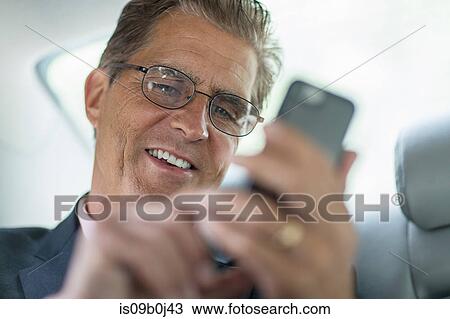 Mature businessman in back of car, using smartphone View Large Photo Image Stock Image - Mature businessman in back of car, using smartphone. Fotosearch
