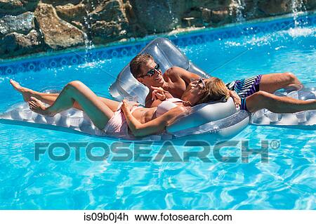 Stock Image - Mature couple in swimming pool, relaxing on inflatables. Fotosearch