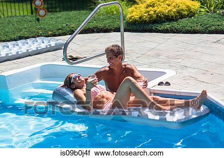 Stock Image - Mature couple in swimming pool, woman relaxing on inflatable. Fotosearch