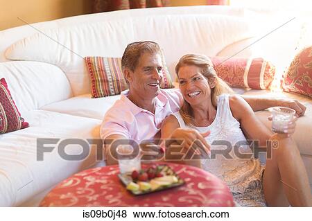 Mature couple relaxing at home, holding drink, eating strawberries View Large Photo Image Stock Photo - Mature couple relaxing at home, holding drink, eating strawberries. Fotosearch