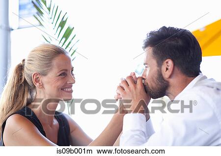 Picture - Mature couple sitting outdoors, man kissing woman's hands, smiling. Fotosearch