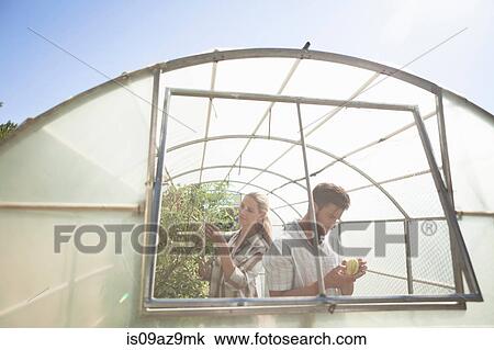 Stock Image - Mature couple tending to plants in greenhouse. Fotosearch