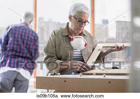 Stock Image - Mature female carpenter sanding picture frame in furniture making workshop. Fotosearch