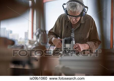 Stock Image - Mature female carpenter using sander in furniture making workshop. Fotosearch