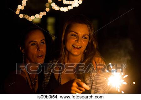 Picture - Mature female friends playing with sparkler in garden at night. Fotosearch