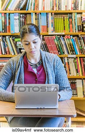 Stock Image - Mature female student using laptop in library. Fotosearch
