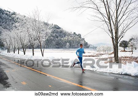 Stock Image - Mature male runner running on road in winter, Lake Kawaguchiko, Mount Fuji, Japan. Fotosearch