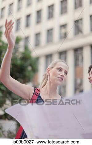 Stock Photo - Mature man and woman outdoors, holding blueprints, having discussion. Fotosearch