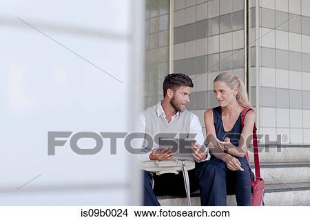 Mature man and woman sitting outdoors, looking at digital tablet View Large Photo Image Picture - Mature man and woman sitting outdoors, looking at digital tablet. Fotosearch