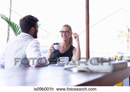 Stock Image - Mature man and woman, sitting outside cafe, drinking coffee, face to face, smiling. Fotosearch