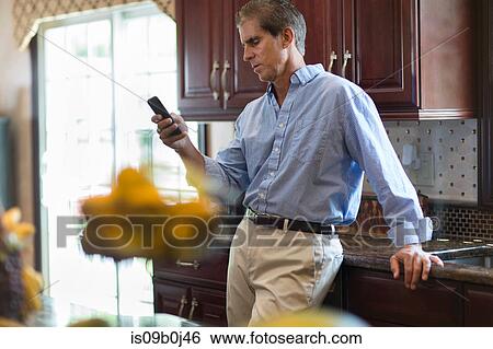 Mature man in kitchen, using smartphone View Large Photo Image Stock Photograph - Mature man in kitchen, using smartphone. Fotosearch