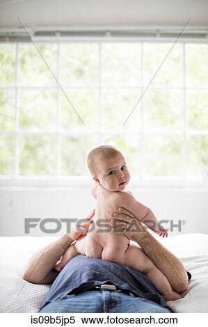 Stock Photography - Mature man lying on bed, baby daughter sitting on his stomach. Fotosearch