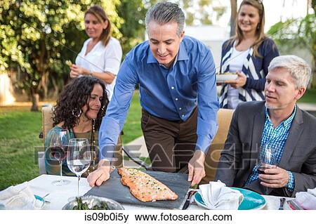 Mature man placing fish cuisine on garden party table View Large Photo Image Stock Photo - Mature man placing fish cuisine on garden party table. Fotosearch