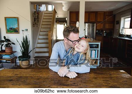 Mature man sitting at kitchen table kissing daughter on cheek View Large Photo Image Stock Image - Mature man sitting at kitchen table kissing daughter on cheek. Fotosearch