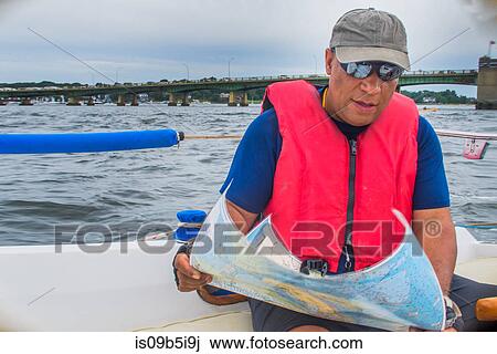 Stock Image - Mature man sitting on boat, looking at map. Fotosearch