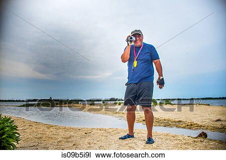 Mature man standing on beach looking through camcorder View Large Photo Image Stock Image - Mature man standing on beach looking through camcorder. Fotosearch