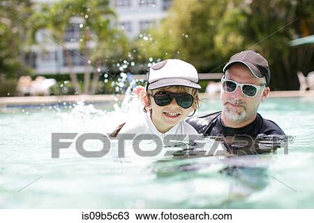 Stock Image - Mature man teaching son in outdoor swimming pool. Fotosearch