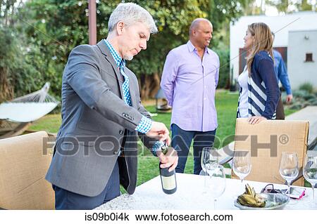 Mature man uncorking wine bottle at garden party table View Large Photo Image Stock Image - Mature man uncorking wine bottle at garden party table. Fotosearch