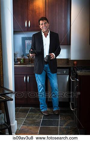 Mature man wearing suit jacket and jeans in kitchen, holding digital tablet and coffee mug, looking at camera smiling View Large Photo Image Stock Photo - Mature man wearing suit jacket and jeans in kitchen, holding digital tablet and coffee mug, looking at camera smiling. Fotosearch