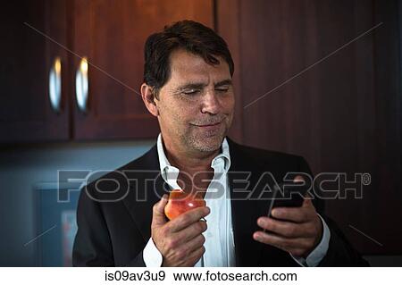 Mature man wearing suit jacket holding apple, looking at smartphone smiling View Large Photo Image Stock Photo - Mature man wearing suit jacket holding apple, looking at smartphone smiling. Fotosearch