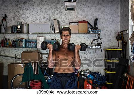 Stock Image - Mature man working out in garage, lifting weights. Fotosearch