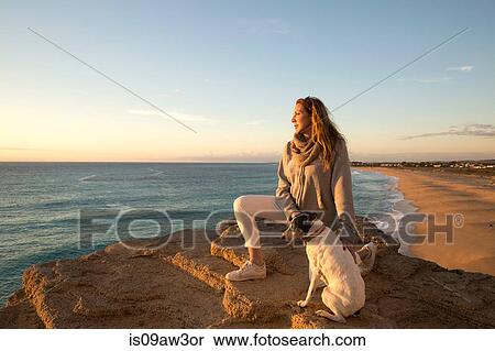 Stock Photography - Mature woman and dog looking out to sea from cliff rock, Conil de la Frontera, Spain. Fotosearch