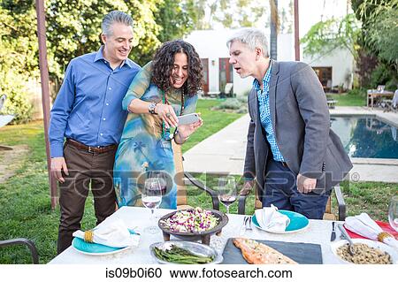 Stock Image - Mature woman photographing garden party table on smartphone. Fotosearch