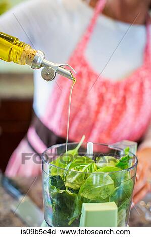 Mature woman pouring olive oil into food processor containing basil, making pesto sauce, mid section View Large Photo Image Stock Image - Mature woman pouring olive oil into food processor containing basil, making pesto sauce, mid section. Fotosearch
