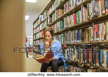 Stock Photo - Mature woman reading book from library shelves. Fotosearch